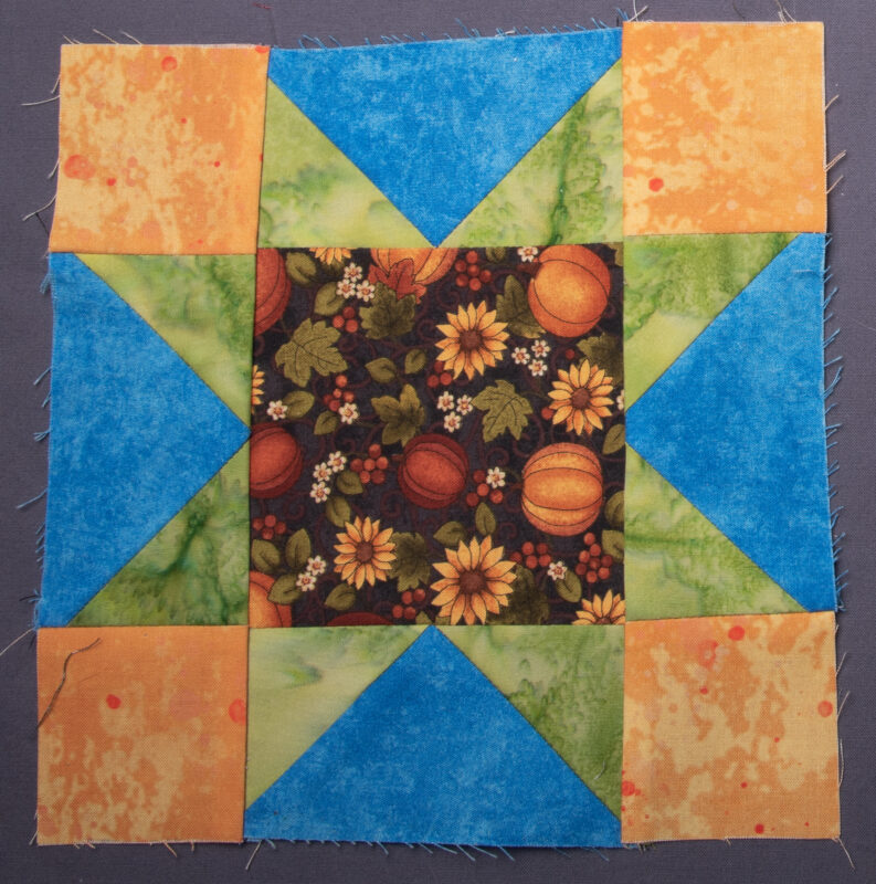 Variable Star quilt block featuring a fall print with pumpkins and sunflowers in the middle