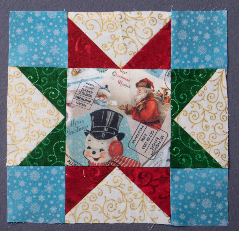 Variable star block, with a fussy cut Christmas image in the center, featuring a snowman and Santa Claus. The corners are blue with white snowflakes, and the stars are red and green with a white background.