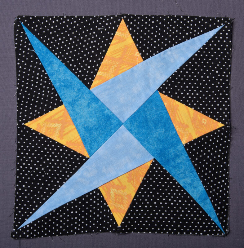 Starry Path quilt block, with blue and gold arms and a black polka dot background